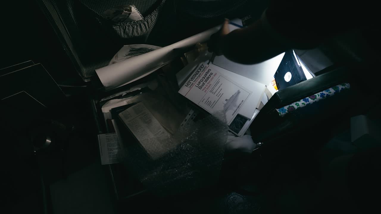 Person with torchlight searches family memorabilia in attic trunk
