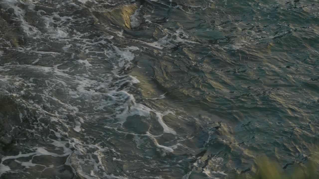 Dynamic aerial footage of powerful ocean waves with churning white foam and dark water. Natural seascape captures raw maritime energy along the Gijon coast with dramatic texture and movement.