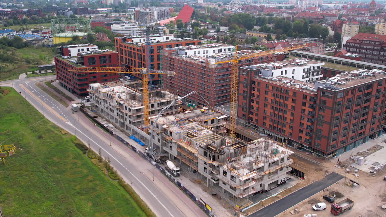 vista aérea de un bullicioso sitio de construcción adyacente a modernos edificios de apartamentos de ladrillo en gdansk, con vehículos navegando por la carretera de la ciudad