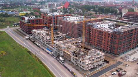 Aerial view of a bustling construction site adjacent to modern brick apartment buildings in Gdansk, with vehicles navigating the city road