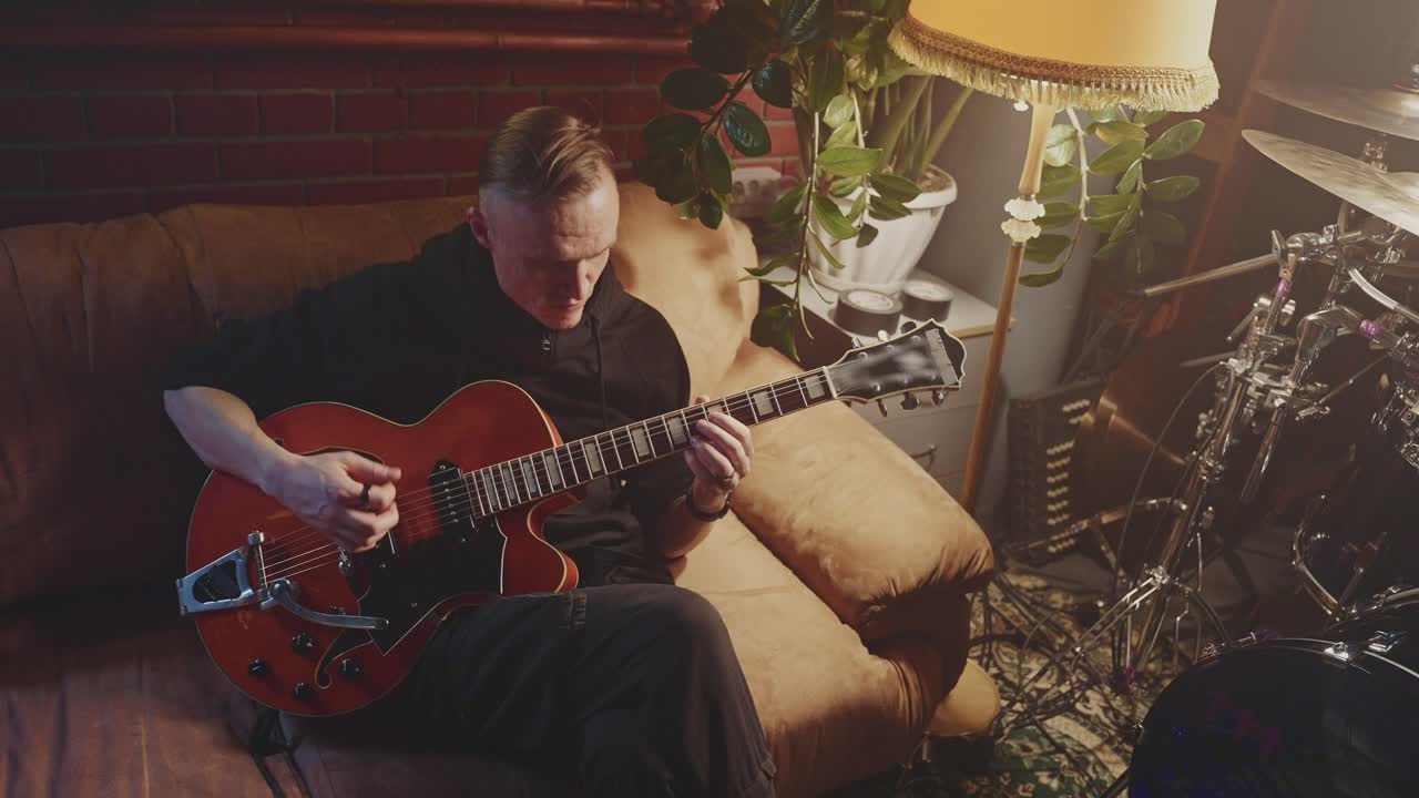 Mand spiller guitar i et hjemmestudie
