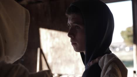 a young teenage boy looks over at a man in a white hooded cloak, acting as jesus