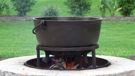 an old fashioned iron kettle over the fire of an outdoor campfire