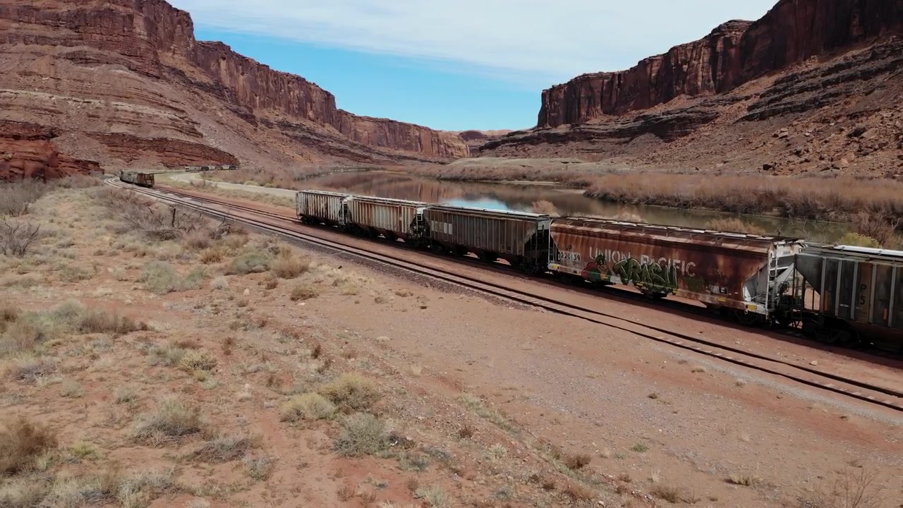 Et 4K droneoptagelse af stejle klipper og en jernbanestrækning, der løber langs Colorado River, skærende gennem det unikke og barske ørkenlandskab nær Moab, Utah.