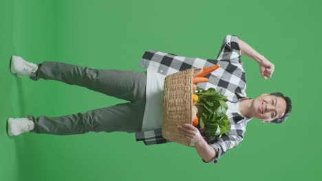 cuerpo lleno de granjero masculino asiático con canasta de verduras sonrisa y flexión del músculo en el fondo de la pantalla verde en el estudio