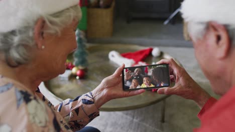 Lächelndes-Kaukasisches-älteres-Paar,-Das-Sein-Smartphone-Für-Einen-Weihnachtsvideoanruf-Mit-Der-Familie-Auf-Dem-Bildschirm-Nutzt