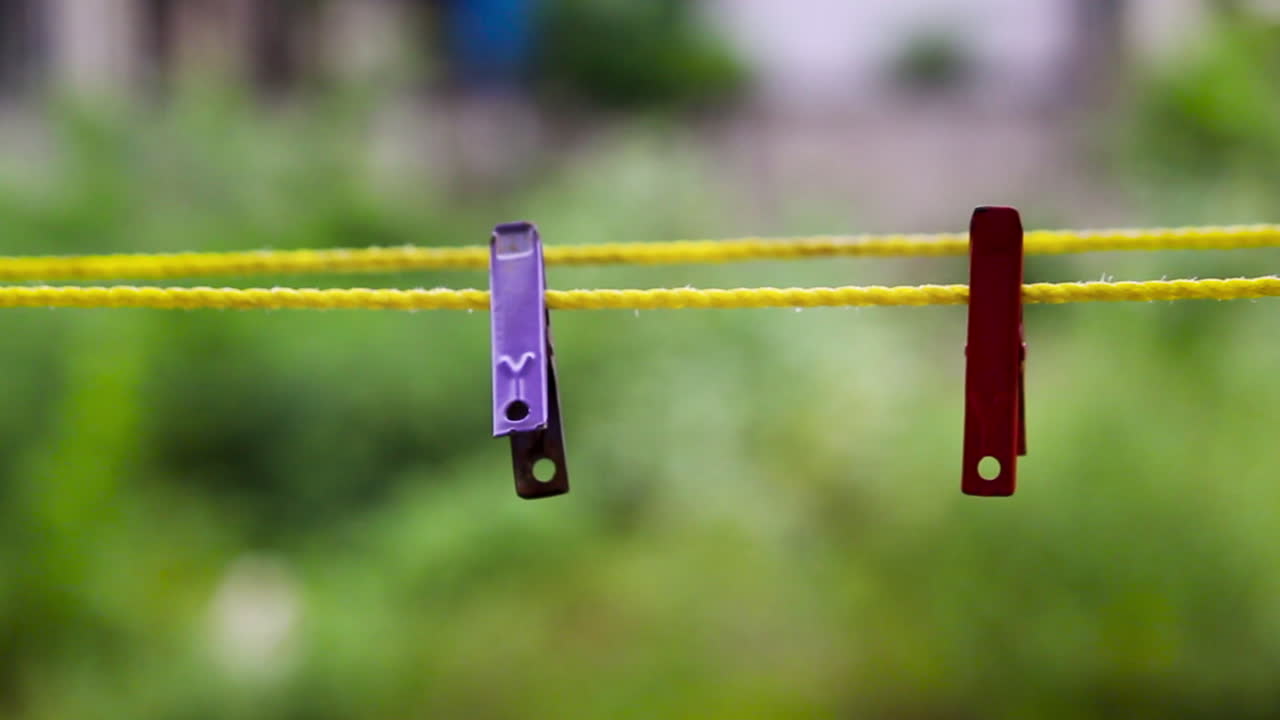 Closeup view of colorful clothespins hanging on yellow rope with blurred green garden background. Perfect for lifestyle, household and minimal concept footage