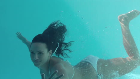 bruneta sonriente nadando bajo el agua y mirando a la cámara