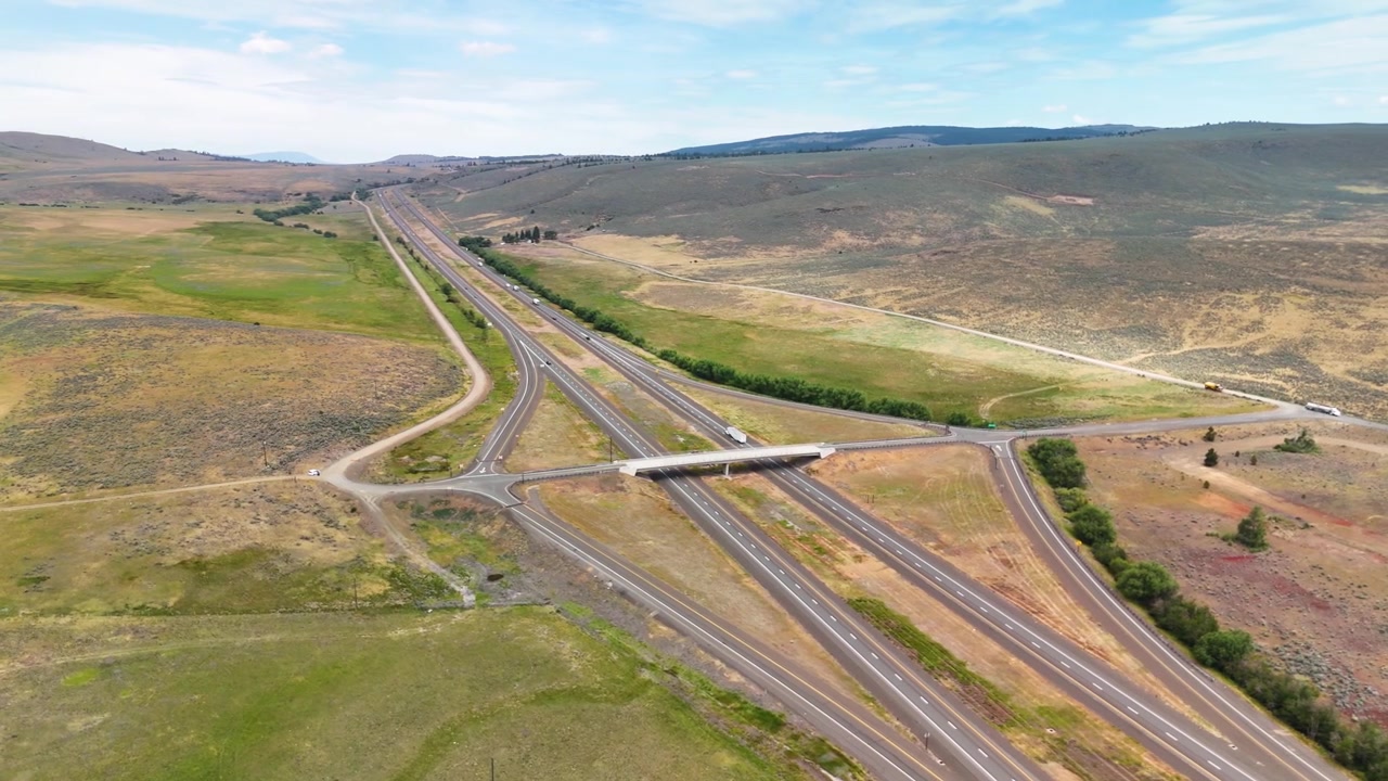 Ripresa cinematografica dall'alto con drone rivela una solitaria autostrada americana che attraversa pianure smeraldo sconfinate, seguendo la strada dritta infinita circondata da maestosi paesaggi verdi dall'alto