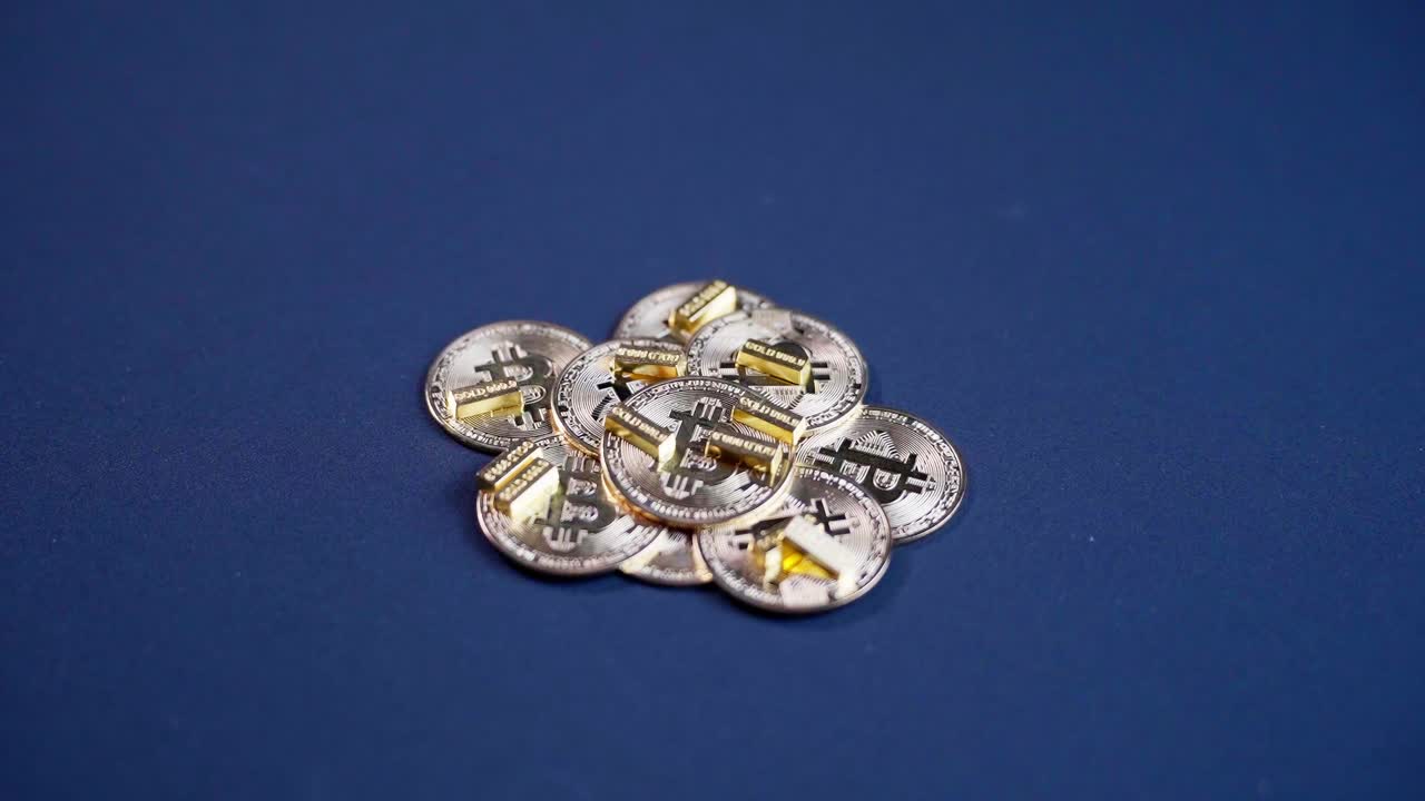 Pile of bitcoin, or digital gold, centered on blue table with small gold bars.