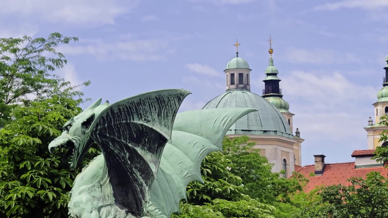 Panorâmica da Estátua do Dragão da Ponte do Dragão até a Catedral de Liubliana, também conhecida como Catedral de São Nicolau, com Árvores Verdes e Telhados da Cidade Antiga
