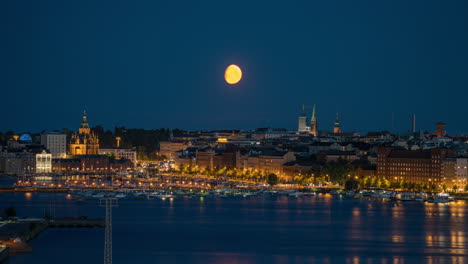 Timelapse-of-the-moon-set-above-the-illuminated-skyline-of-Helsinki,-blue-hour