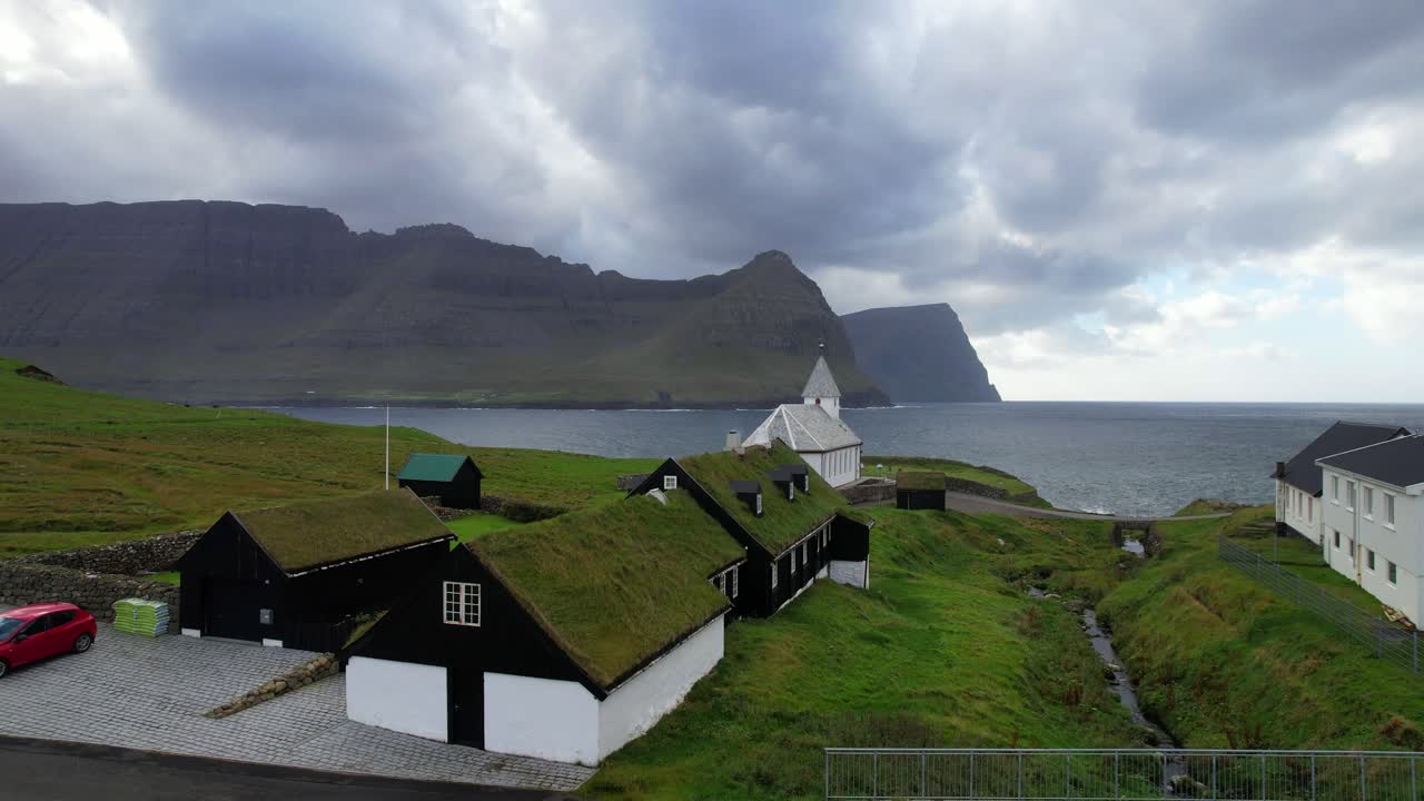 casas con techo de césped verde de vidareidi con iglesia frente al mar, vidoy, islas feroe