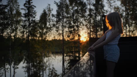 joven rubia disfruta de la vista del lago al atardecer en la relajante cabaña de verano nórdico, escena de vacaciones escandinava