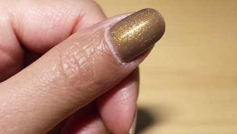 close-up sequence of gold nail polish being applied to a fingernail with precision.