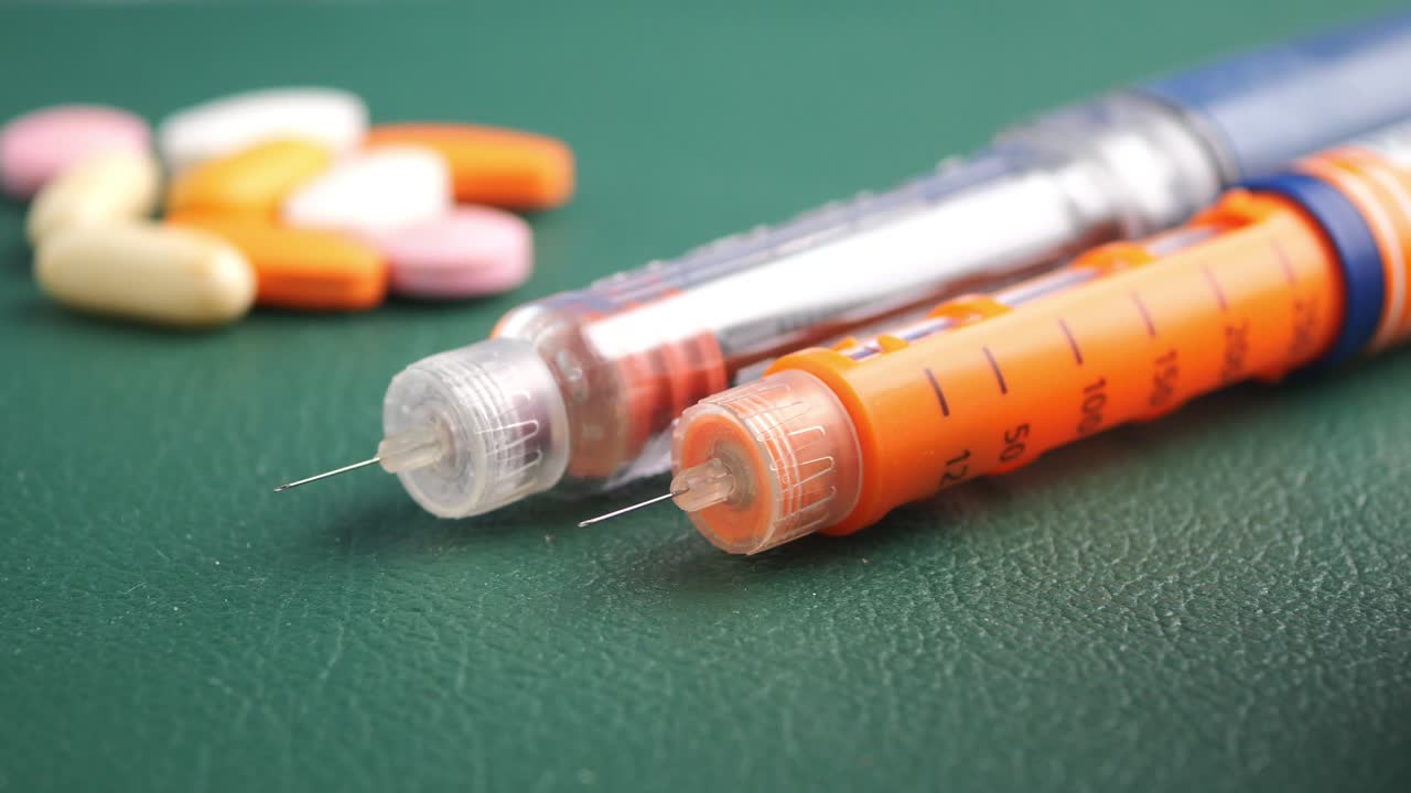 Insulin pens and various medications on a green surface