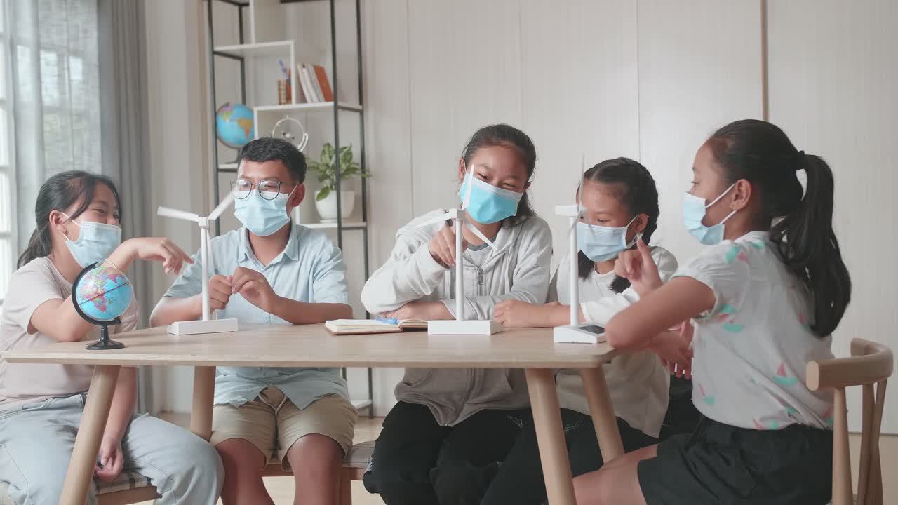 Middle School Classroom: Asian Kids Are Wearing Facemasks Learning About Ecology Problems And Their Solution With Wind Turbine Model And Globe At School