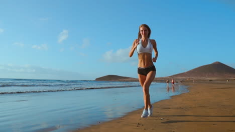 Beautiful-sportive-woman-running-along-beautiful-sandy-beach,-healthy-lifestyle,-enjoying-active-summer-vacation-near-the-sea.-in-slow-motion
