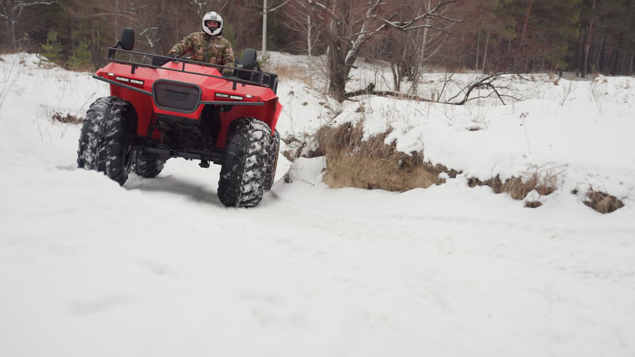 ATV rosso si lancia contro un banco di neve, primo piano d'azione mostra il battistrada aggressivo che morde le derive ghiacciate, il pilota con casco si fa strada su una radura accidentata, sospensioni che si comprimono, spruzzi di neve e sfoggio di potenza, sentiero.