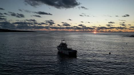 Aerial-view-of-tourist-boat-on-sea-in-front-of-golden-sunset-and-clouds-at-sky-in-the-evening---Australia,-Margaret-River