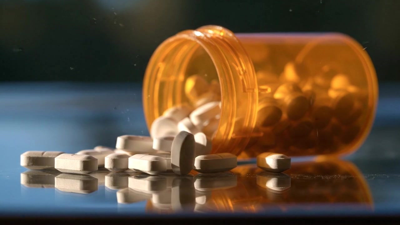 Comprimidos de medicamentos derramando de um frasco âmbar sobre uma superfície escura em filmagem científica detalhada
