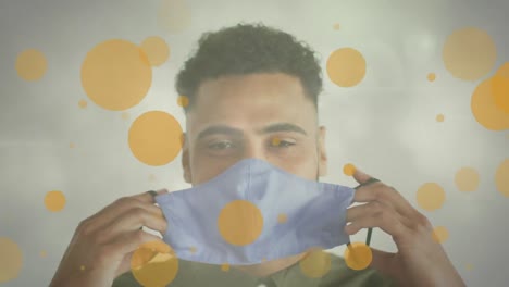 Animation-of-yellow-spots-over-smiling-biracial-man-putting-face-mask-on
