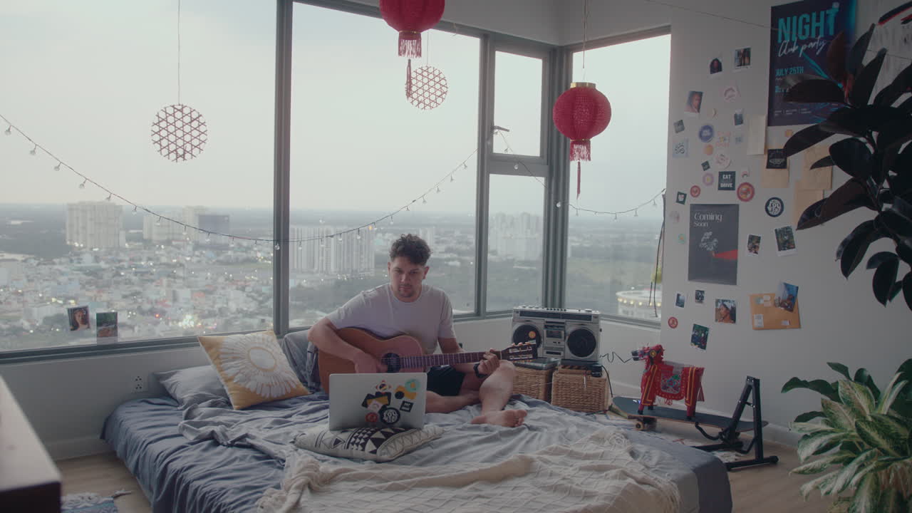 Man Learning Guitar with Video Lessons on Laptop in Bedroom