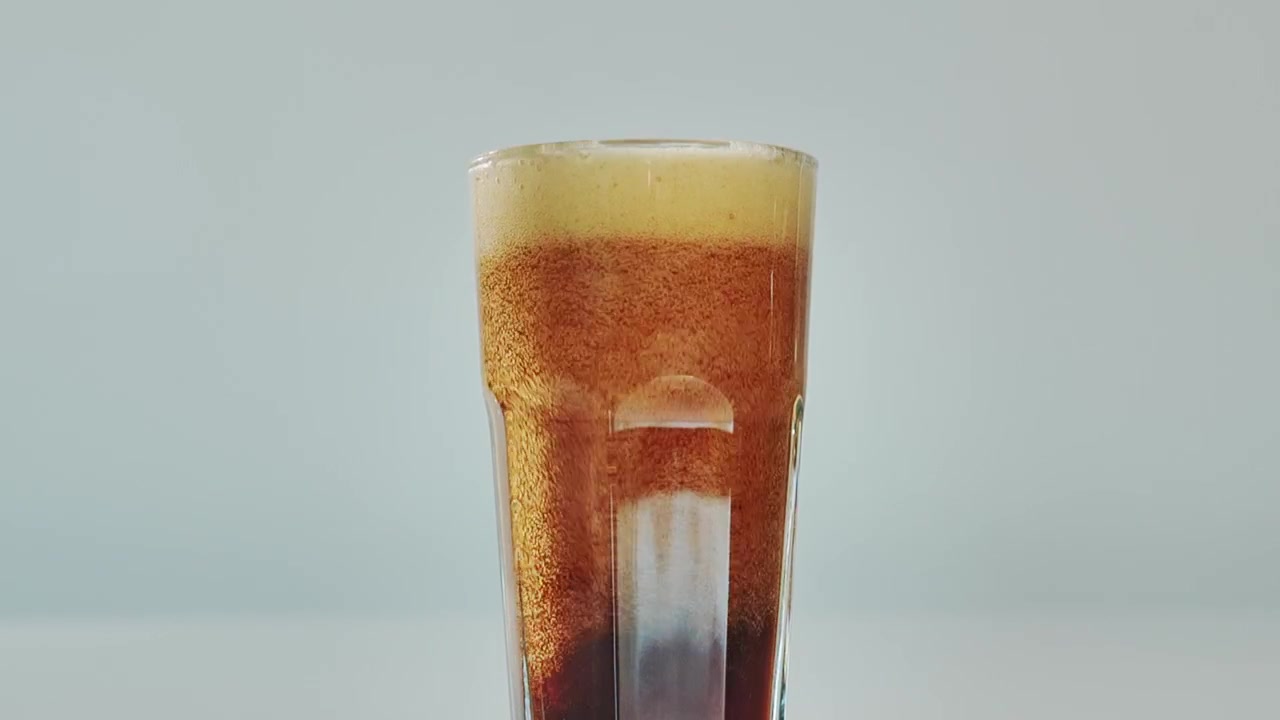 Close-up of fizzy drink, poured into a transparent glass, creating bubbling foam