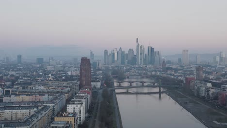 Frankfurt-Skyline-with-Hotel-tower-and-river-main-in-the-foreground-at-dusk-on-a-misty-winter-morning