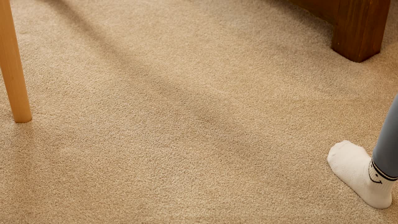 A person vacuums a carpeted room with a handheld vacuum cleaner, showcasing efficient cleaning techniques in a well-lit home environment