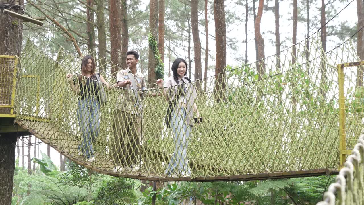 Young Asian Friends Crossing Rope Bridge in Forest Adventure