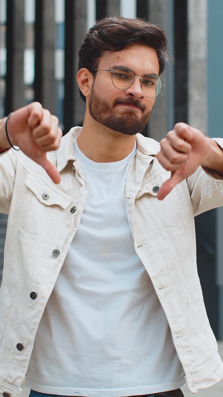 Upset indian man showing thumbs down sign disapproval dissatisfied bad work mistake in urban city