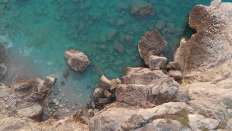 drone-captures-birds-eye-of-rocky-cliff-edge,-camera-flies-over-rugged-landscape-of-blue-water-and-white-sunken-stones