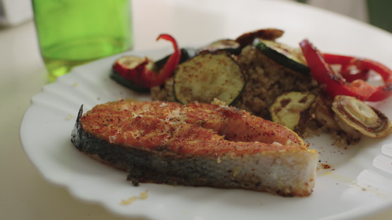 Close-up of a grilled salmon steak served with quinoa and roasted vegetables on a white plate, shot in natural light