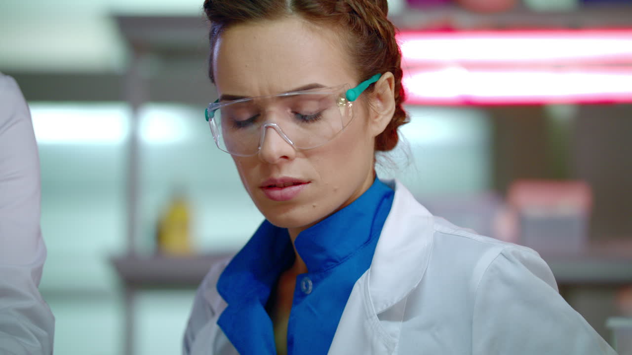 Lab researcher in laboratory. Close up of female scientist in safety glasses