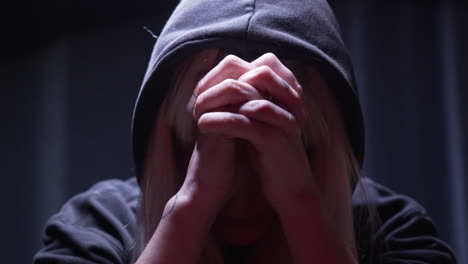 Depressed-person-prays-with-tightly-clenched-hands-with-black-hood-in-a-dark-room