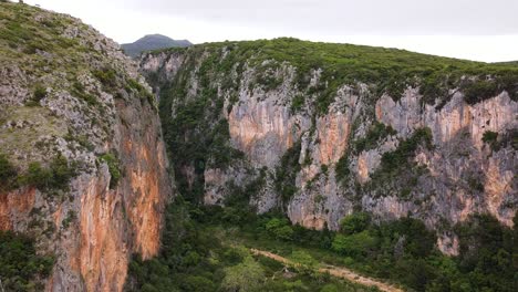 Aerial-view-of-the-stunning-Gjipe-Canyon-with-its-towering-rocky-cliffs-and-lush-greenery,-creating-a-breathtaking-natural-landscape