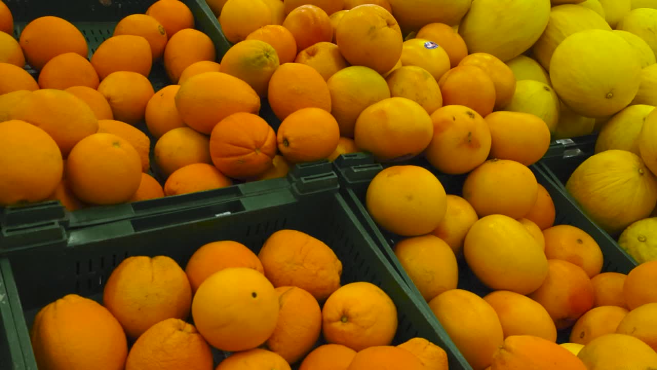 imágenes deslizándose lentamente de hermosas y deliciosas naranjas de color amarillo y naranja vibrante, limones y melones en cajas de plástico verde en un supermercado o una tienda en un estante. la fruta está en una pila