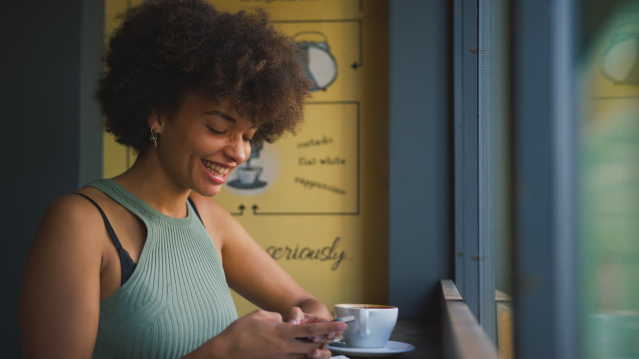 cliente femenina en la ventana de una cafetería enviando mensajes usando un teléfono móvil