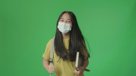 asian girl student wearing a mask, holding book while running to school on green screen chroma key