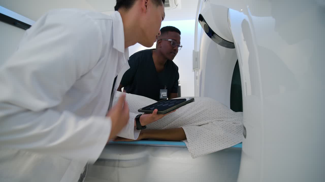Medical staff doing prep checks with clinician checking tablet, placing patient in scanner for CT
