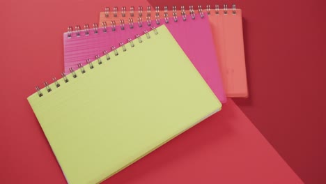 overhead view of colourful notebooks on red background, in slow motion