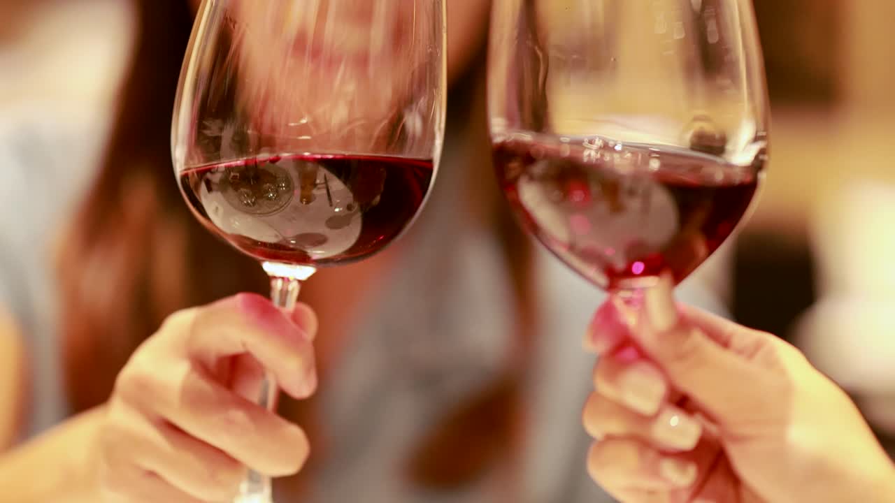 Two people clink glasses of red wine in a warmly lit restaurant, creating a celebratory and intimate atmosphere