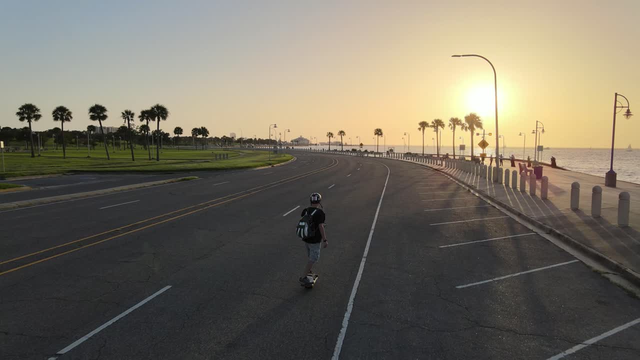 Young Man Skateboarding At Asphalt Lakeshore Drive At Dusk In New Orleans, USA. - aerial follow