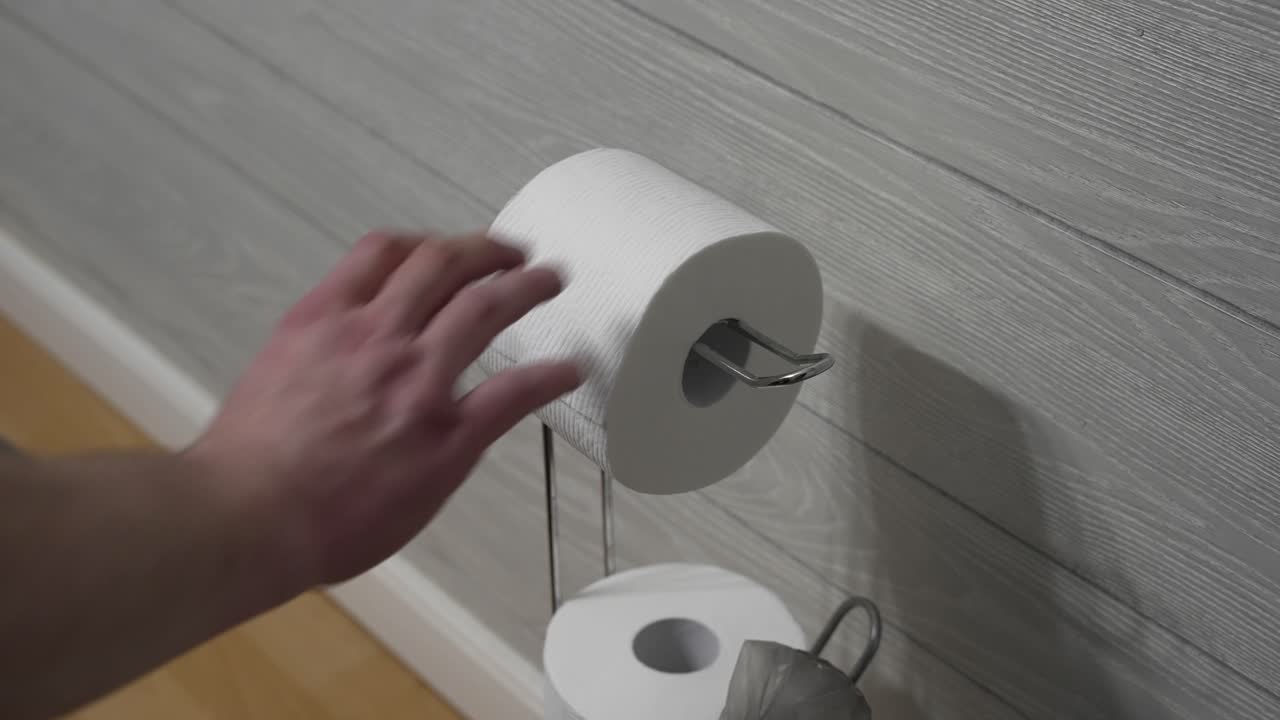 A man pulls a sheet of toilet paper in a bathroom