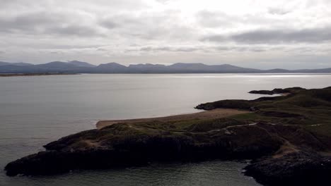 Aerial-view-Ynys-Llanddwyn-island-Anglesey-coastal-walking-trail-with-Snowdonia-mountains-across-the-Irish-sea-panning-left