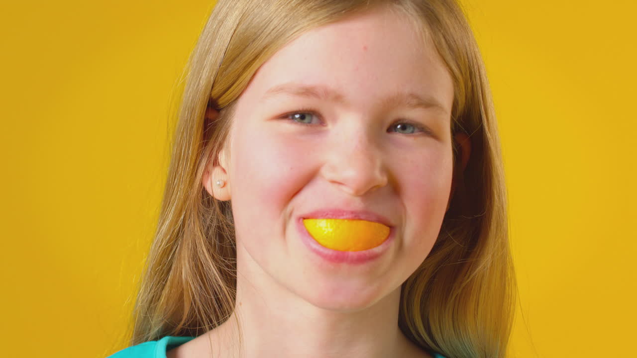 retrato de estudio de una niña usando un segmento naranja para la boca y los dientes contra un fondo amarillo
