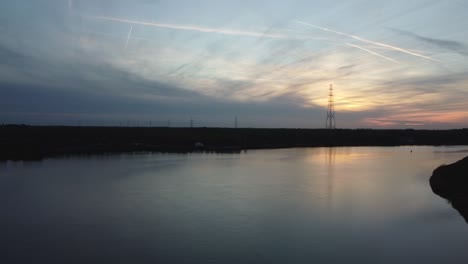 Silueta-De-Poste-De-Línea-Eléctrica-Solitaria-De-Pie-Detrás-Del-Río-Scheldt,-Vuelo-Aéreo-Hacia-La-Vista