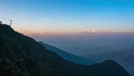 the sun setting over the himalayan mountains and a cable car going up and down the mountain in the foreground