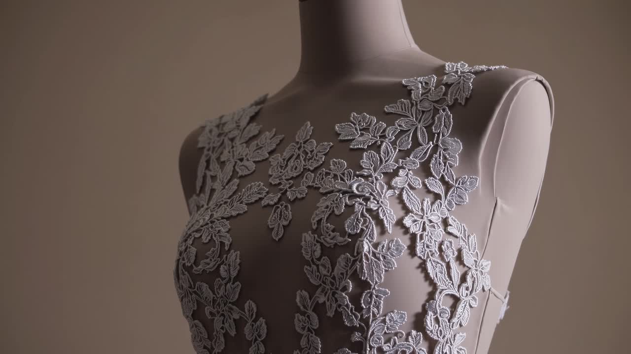 Vídeo em close-up de um manequim exibindo detalhes complexos de renda em um vestido, capturado de lado